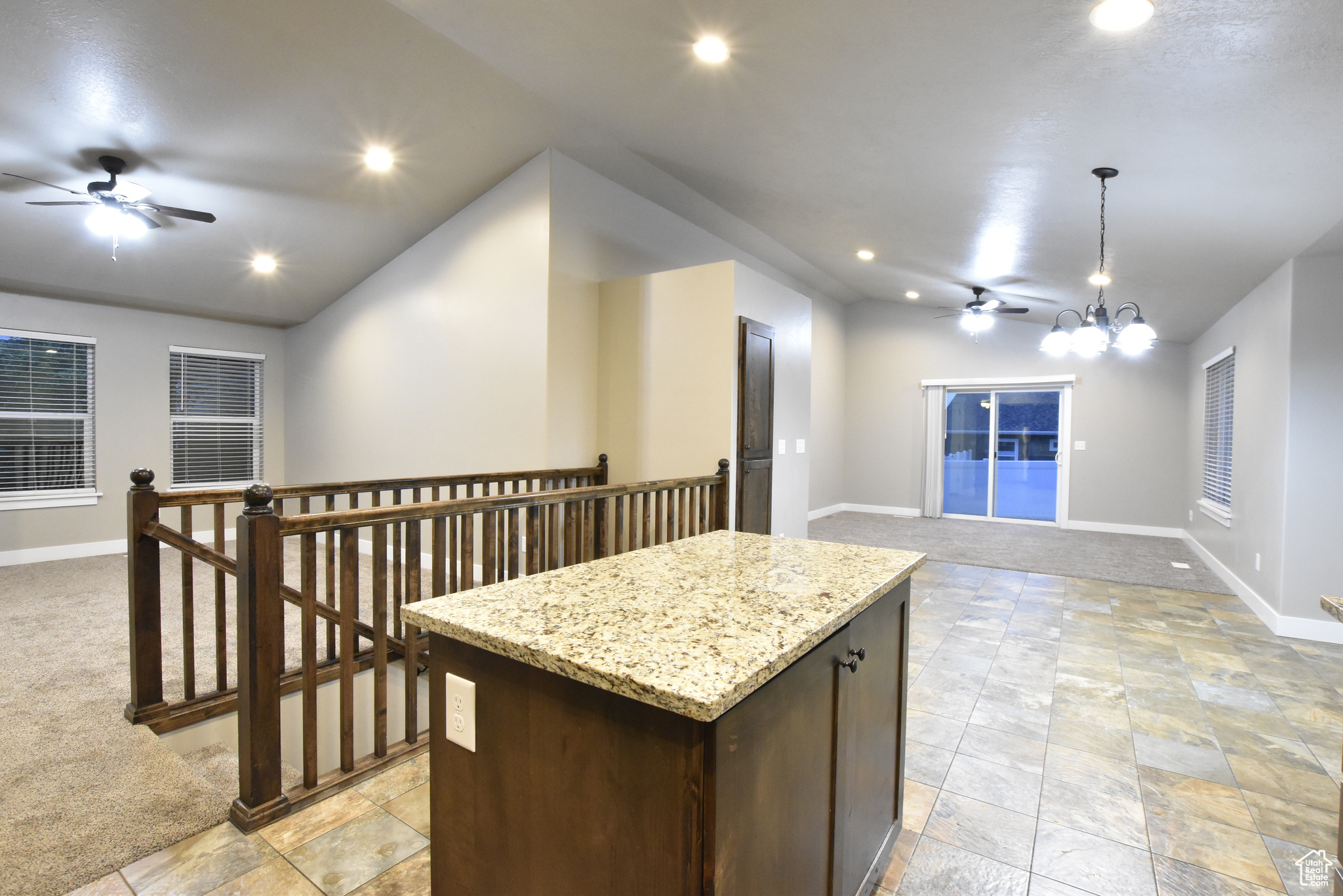 Kitchen with light carpet, dark brown cabinets, ceiling fan with notable chandelier, and a kitchen island