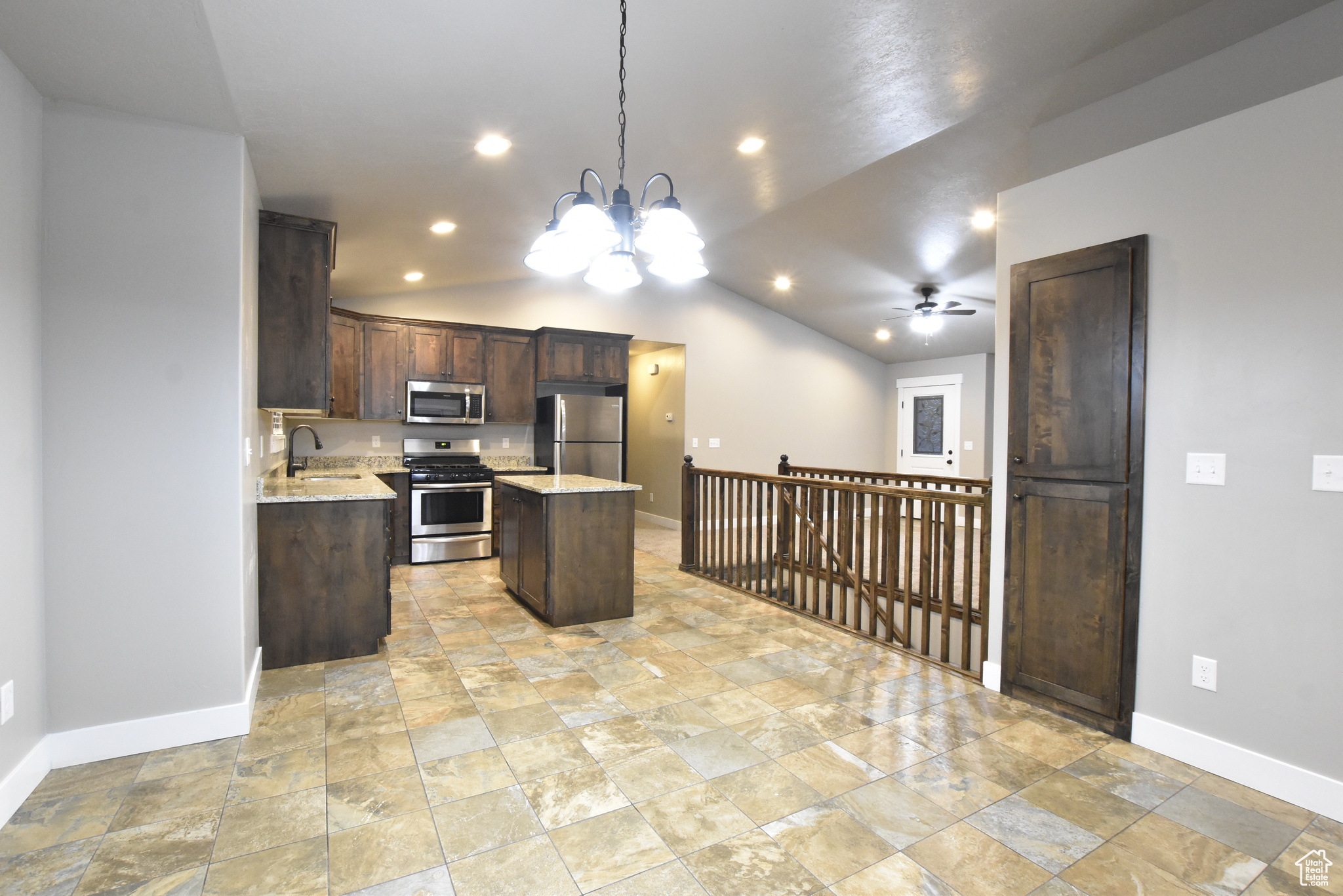 Kitchen featuring stainless steel appliances, hanging light fixtures, ceiling fan with notable chandelier, a center island, and vaulted ceiling