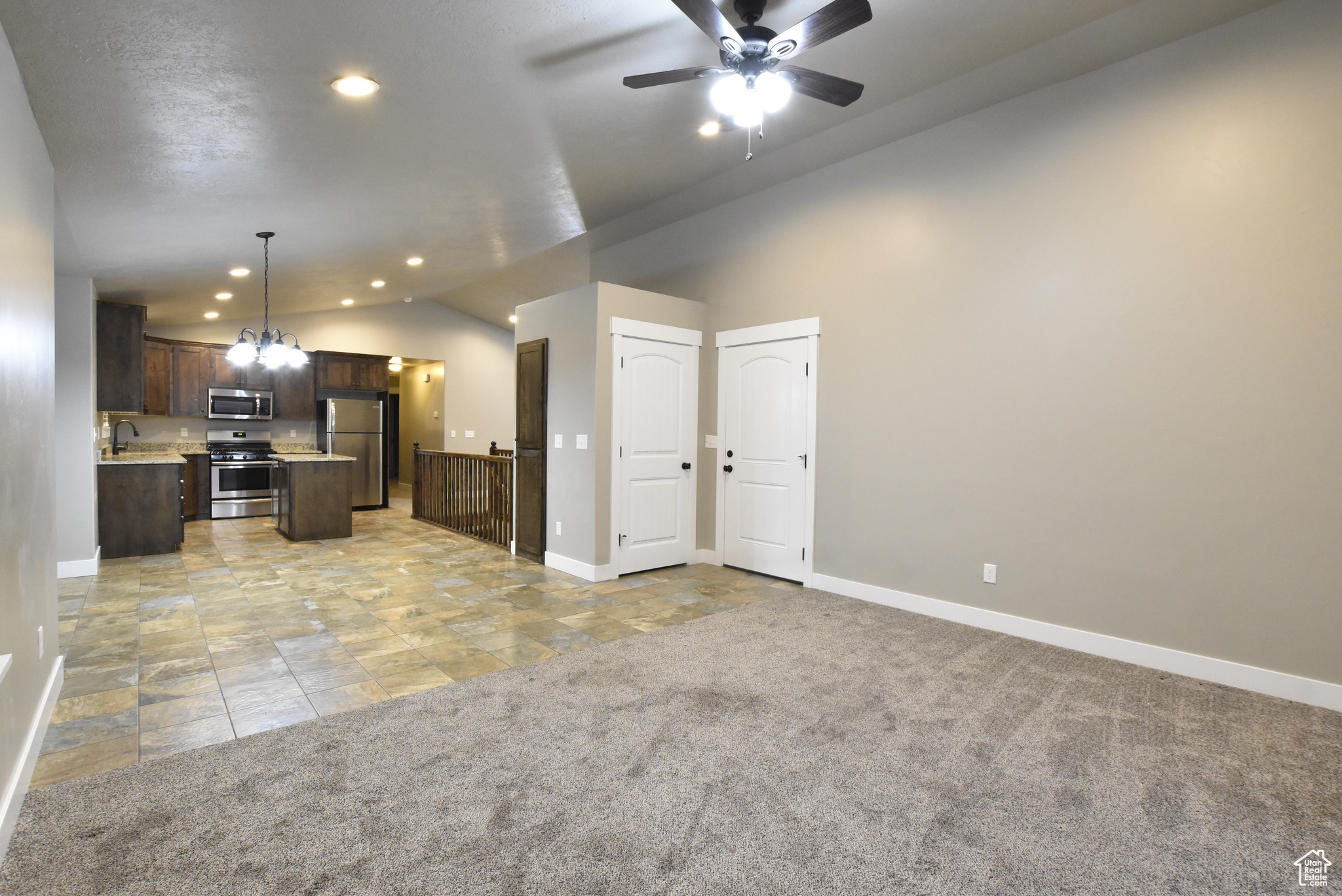 Kitchen featuring appliances with stainless steel finishes, vaulted ceiling, sink, a center island, and light carpet