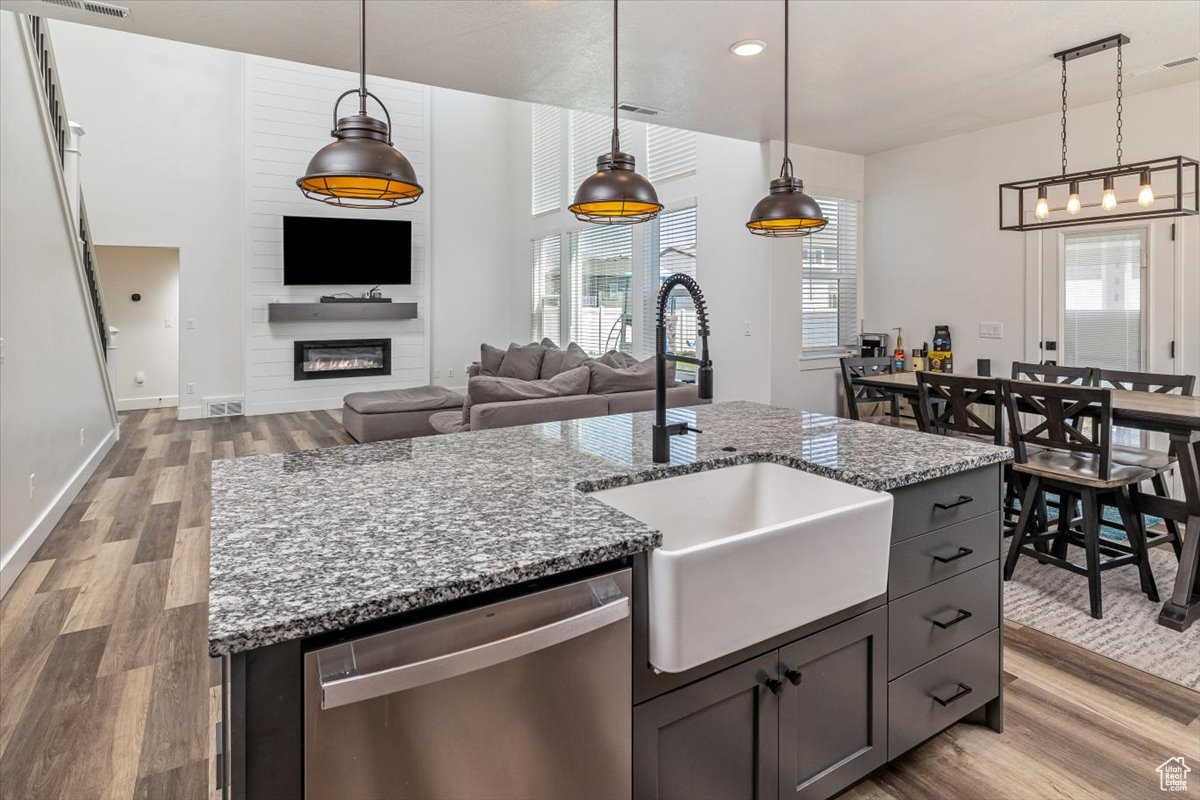 Kitchen featuring hardwood / wood-style flooring, pendant lighting, a kitchen island with sink, and stainless steel dishwasher