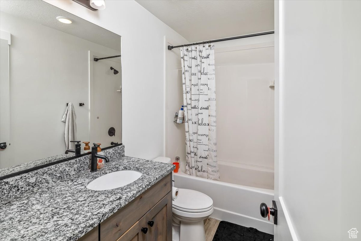 Full bathroom featuring hardwood / wood-style flooring, vanity, shower / tub combo, and toilet