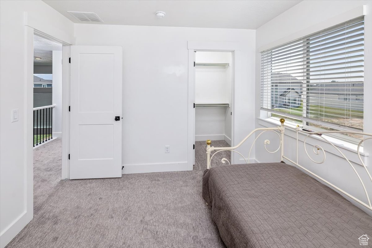 Unfurnished bedroom featuring a walk in closet, a closet, and light colored carpet