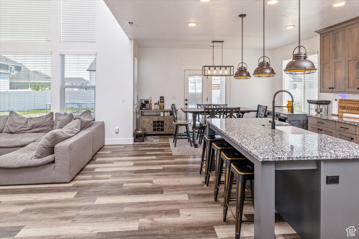 Kitchen with hanging light fixtures, sink, light wood-type flooring, and a kitchen island with sink