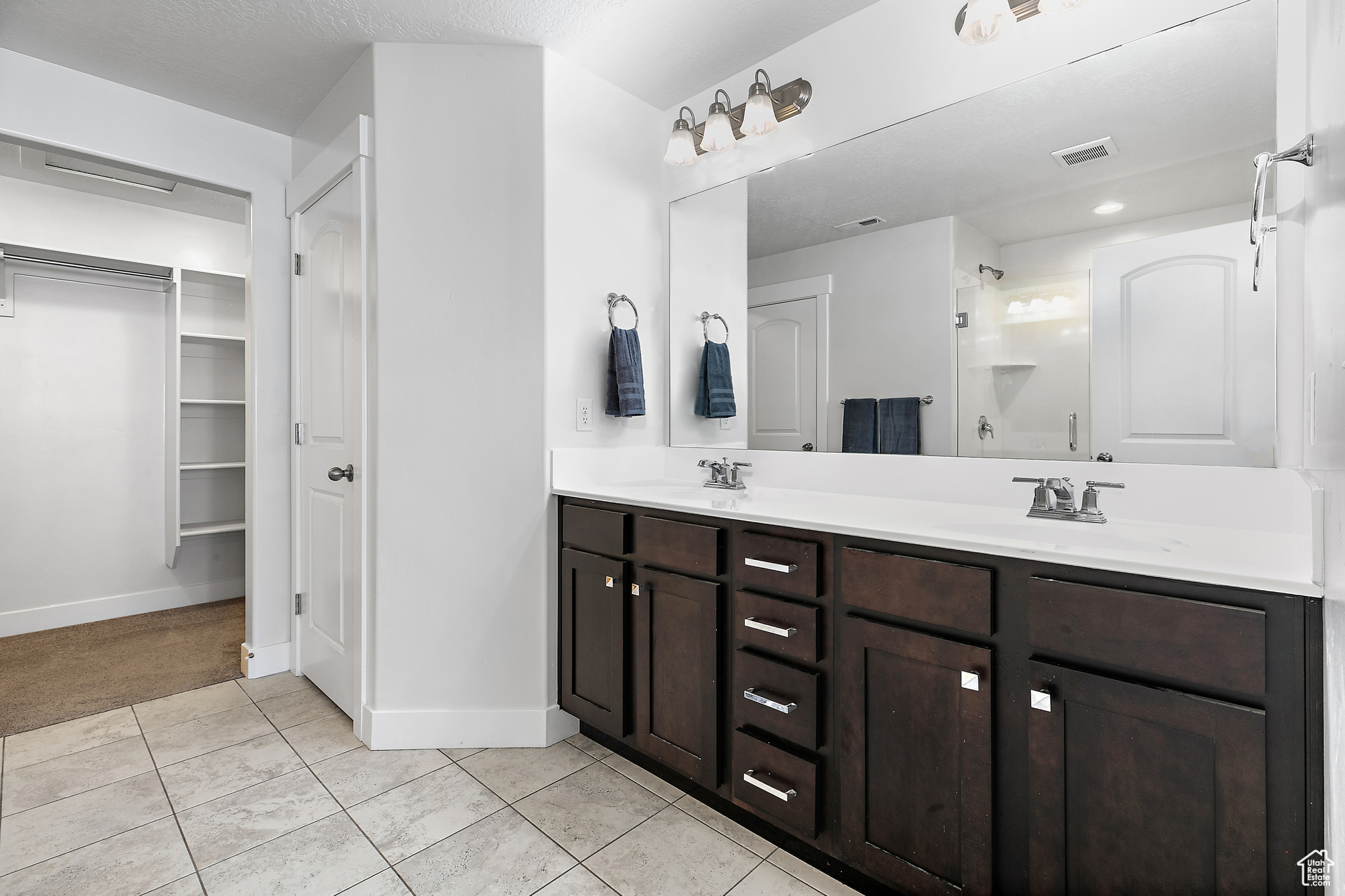 Bathroom with tile patterned floors, dual bowl vanity, and a shower