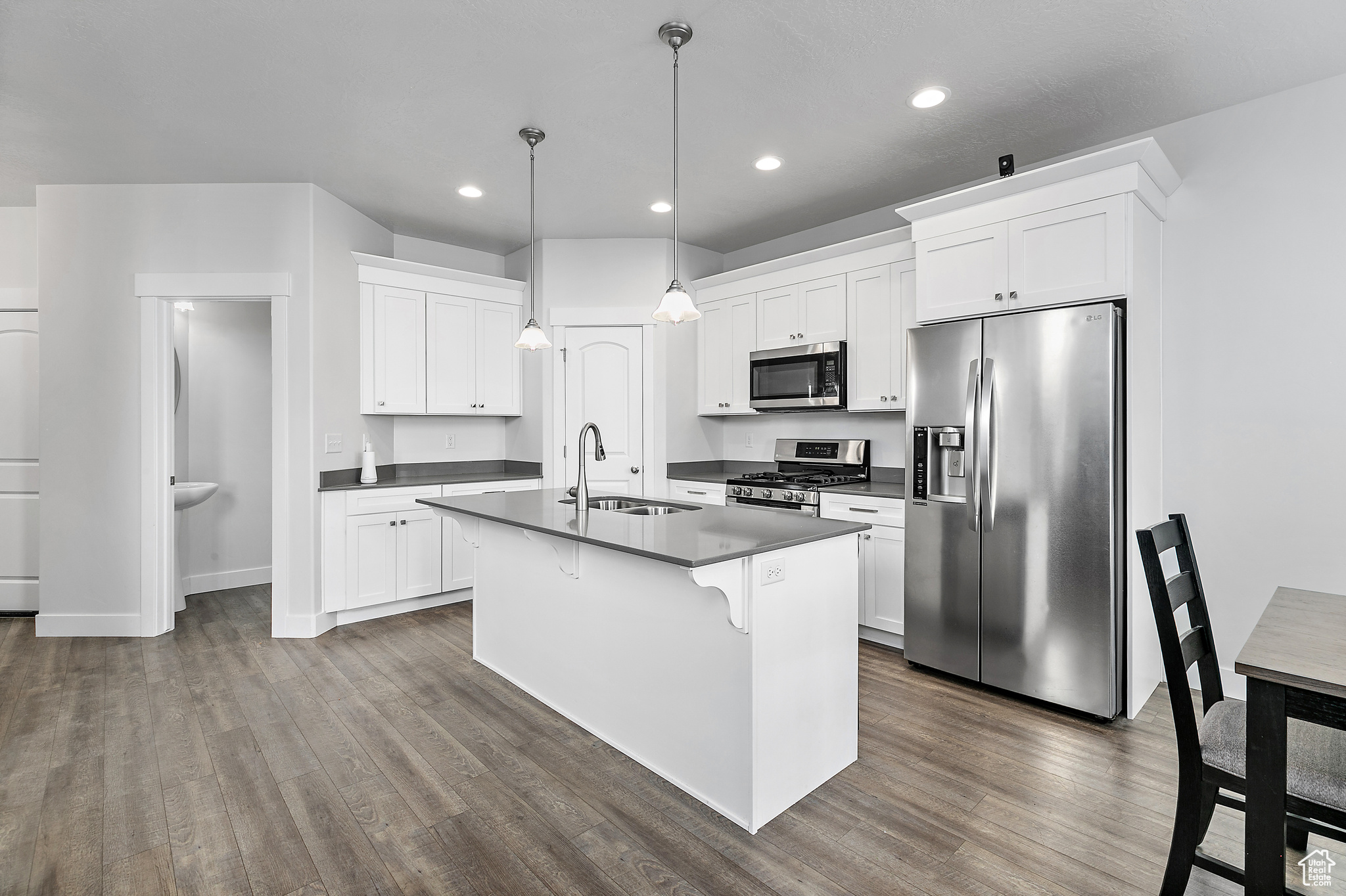 Kitchen featuring white cabinets, wood-style flooring, appliances with stainless steel finishes, and hanging light fixtures