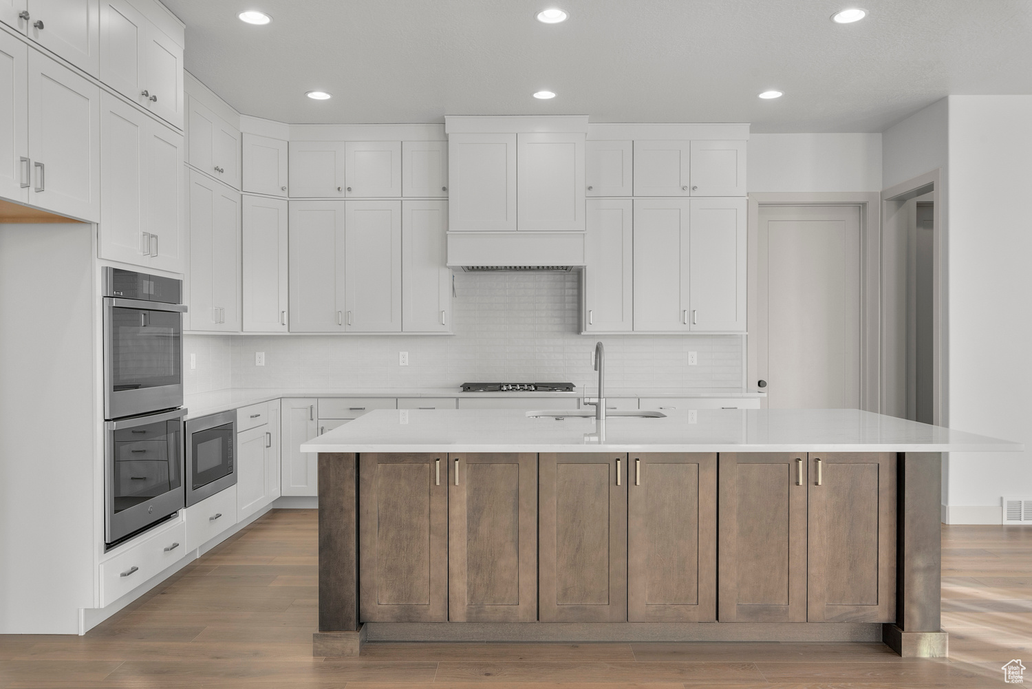 Kitchen with a center island with sink, white cabinetry, and double oven