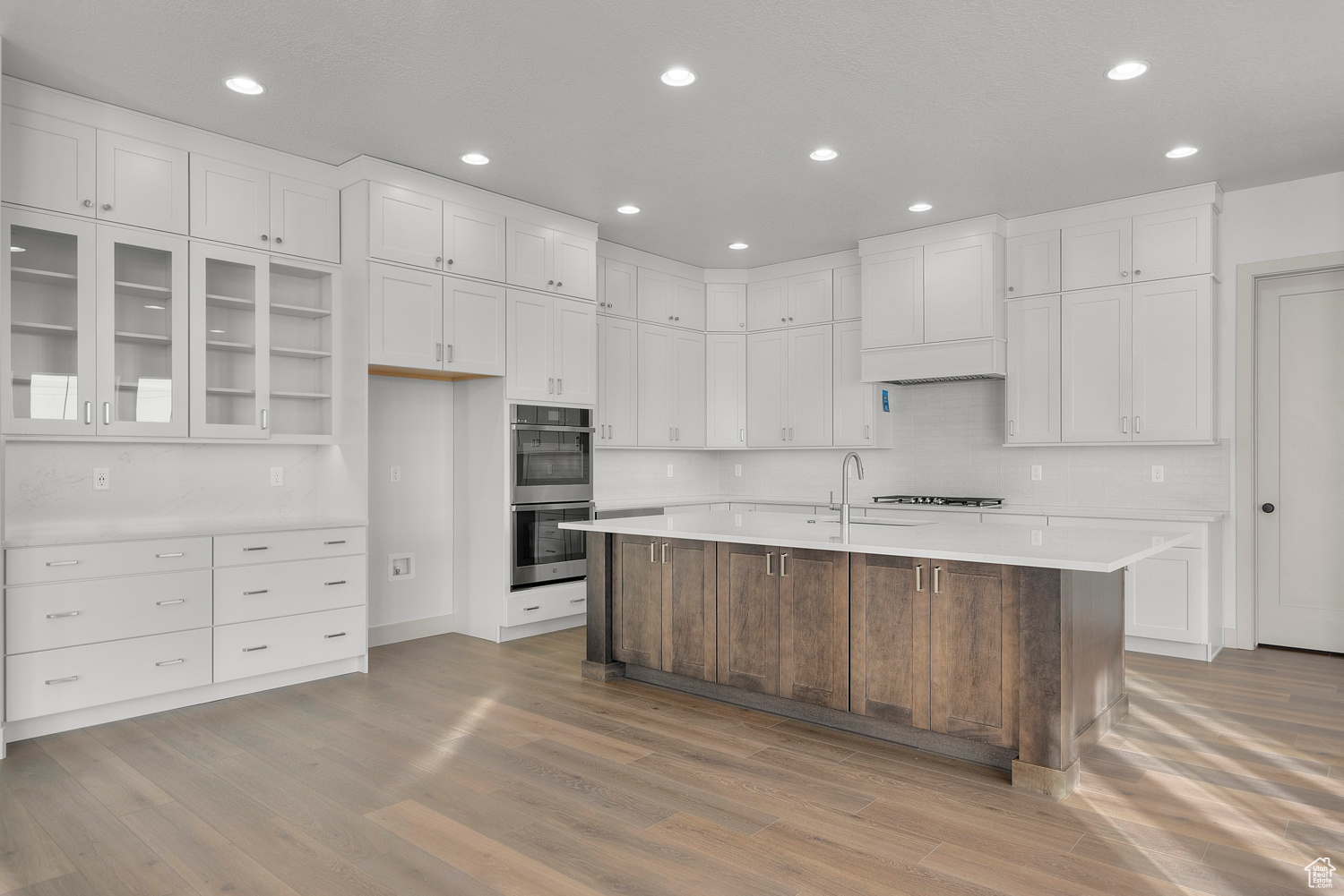 Kitchen with sink, light wood-type flooring, an island with sink, double oven, and white cabinetry