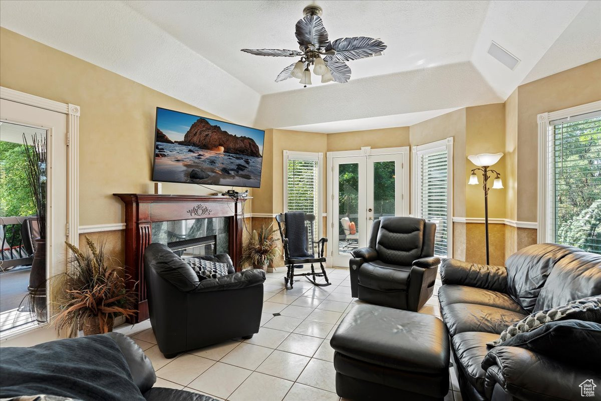 Living room featuring a high end fireplace, french doors, ceiling fan, light tile patterned flooring, and a tray ceiling