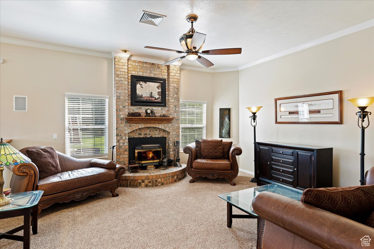 Living room with carpet floors, a fireplace, brick wall, ceiling fan, and ornamental molding