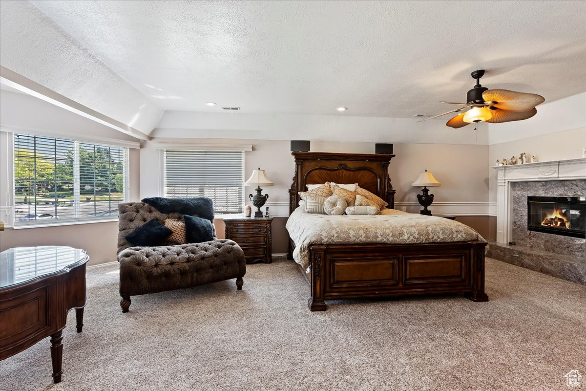 Carpeted bedroom with a premium 2-sided fireplace, a textured ceiling, ceiling fan, and lofted ceiling