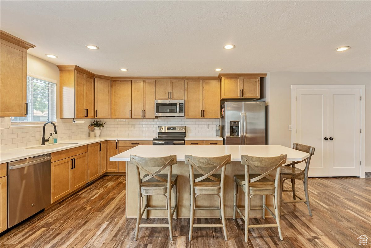 Kitchen with sink, appliances with stainless steel finishes, hardwood / wood-style flooring, and a center island