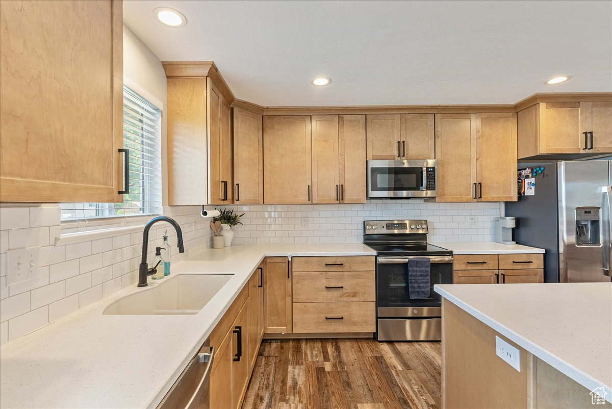 Kitchen with decorative backsplash, sink, stainless steel appliances, and hardwood / wood-style floors