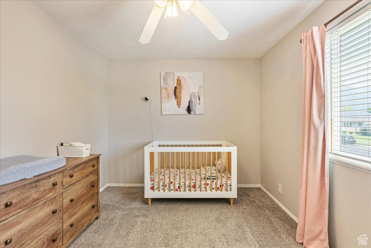 Bedroom with a crib, carpet, multiple windows, and ceiling fan