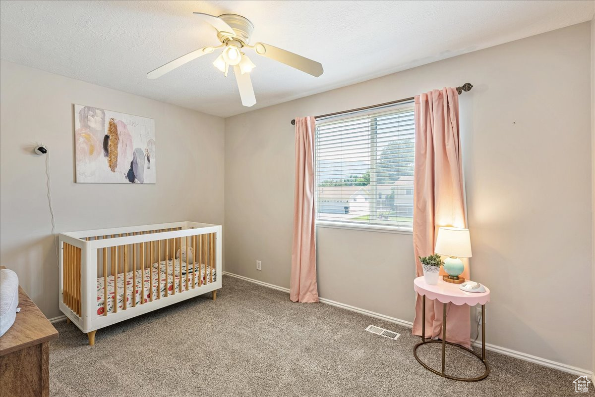 Bedroom with a crib, carpet, and ceiling fan