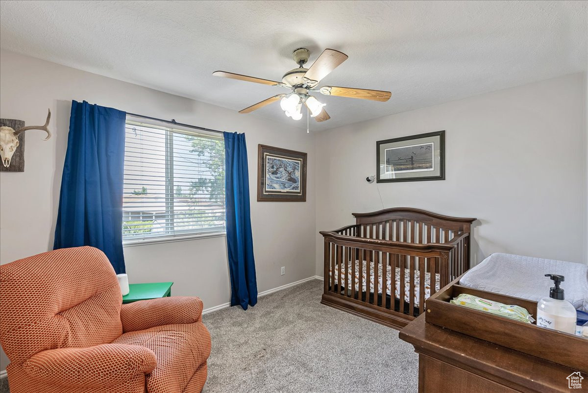 Carpeted bedroom with a crib and ceiling fan