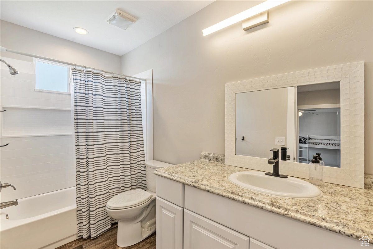 Full bathroom featuring hardwood / wood-style floors, shower / bathtub combination with curtain, toilet, and vanity