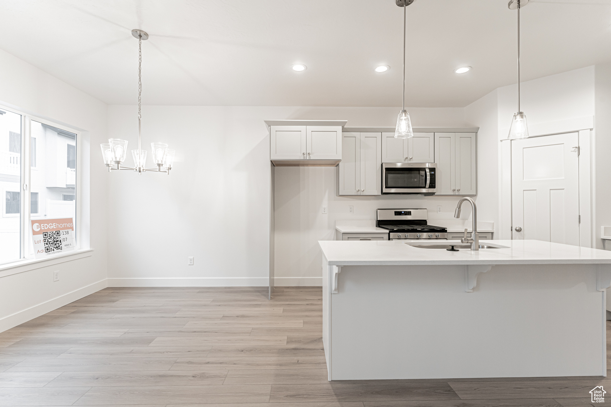 Kitchen with sink, hanging light fixtures, light hardwood / wood-style floors, a kitchen island with sink, and appliances with stainless steel finishes