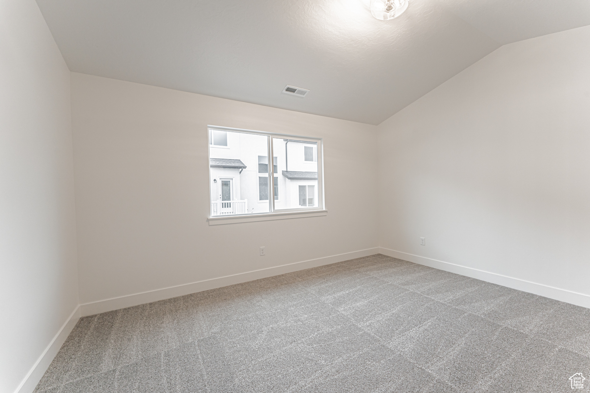 Carpeted spare room featuring vaulted ceiling