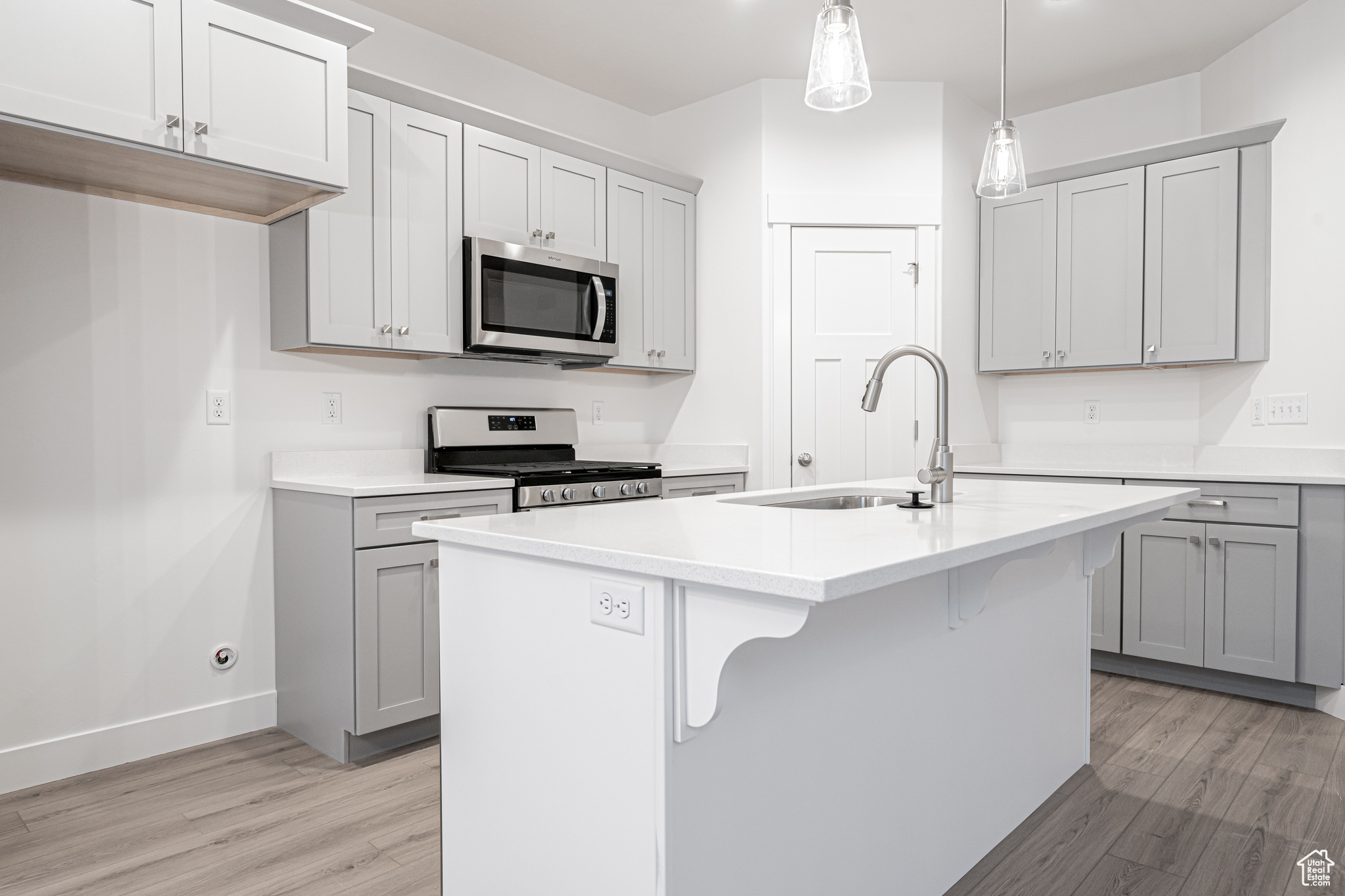 Kitchen with pendant lighting, a center island with sink, range with gas stovetop, and light wood-type flooring