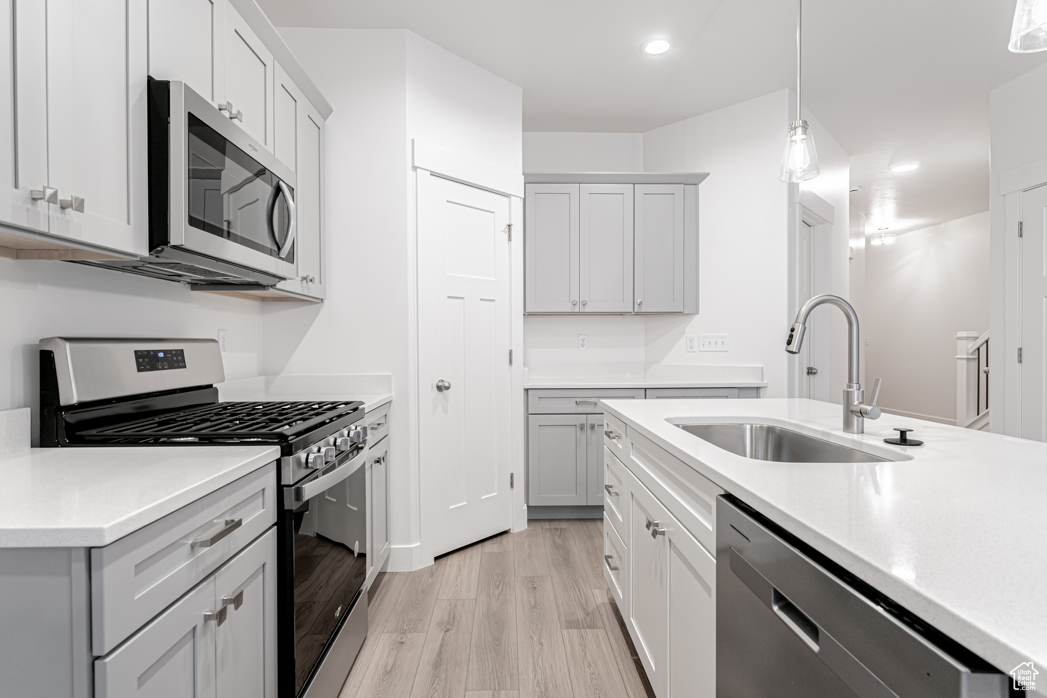 Kitchen with gray cabinetry, sink, decorative light fixtures, light hardwood / wood-style floors, and stainless steel appliances