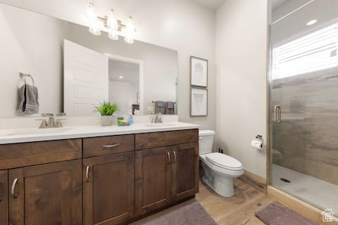 Bathroom with toilet, an enclosed shower, hardwood / wood-style flooring, and dual bowl vanity