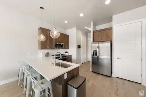 Kitchen with appliances with stainless steel finishes, a breakfast bar area, light hardwood / wood-style flooring, sink, and decorative light fixtures