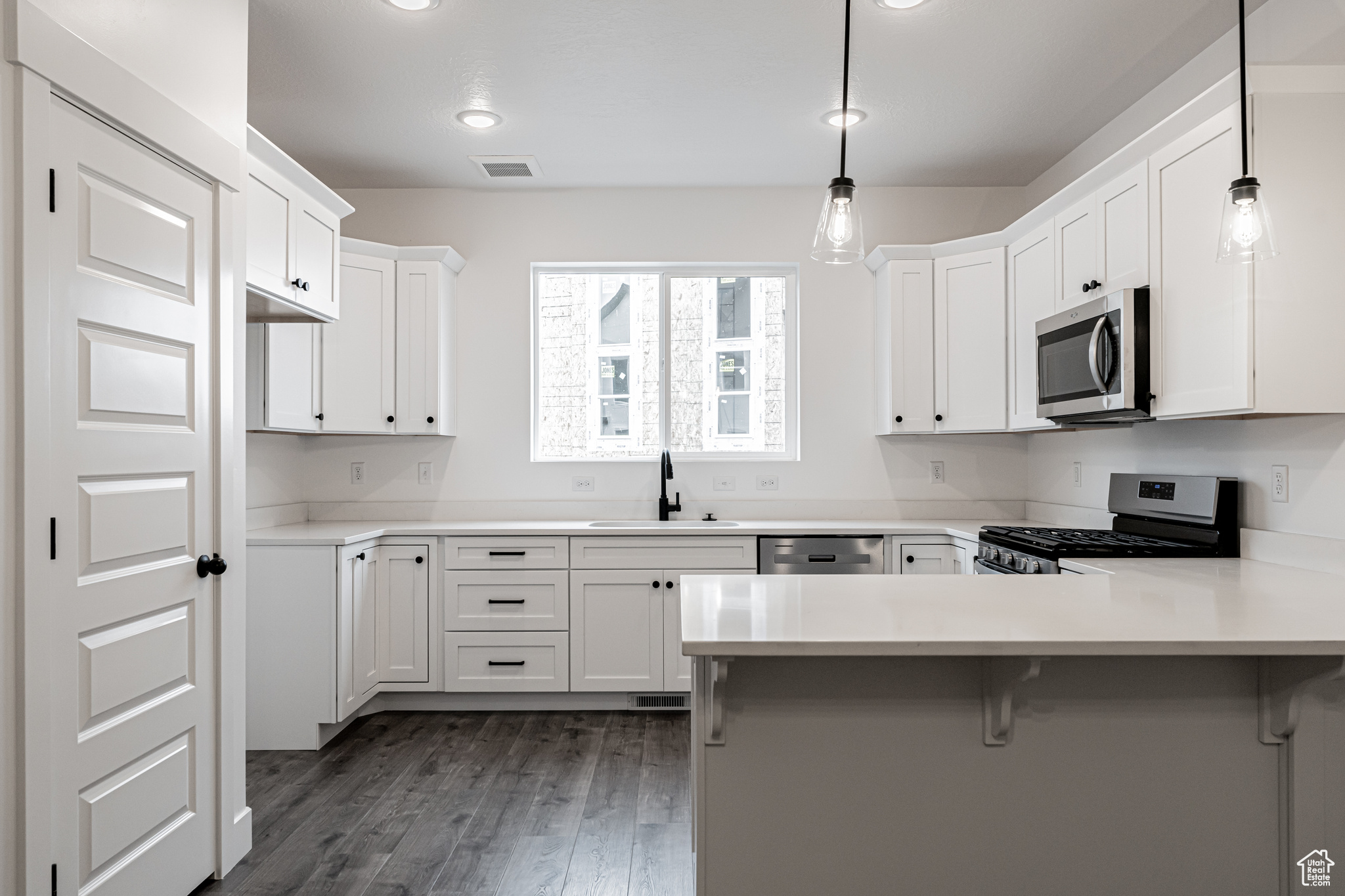 Kitchen featuring white cabinetry, sink, hanging light fixtures, stainless steel appliances, and kitchen peninsula