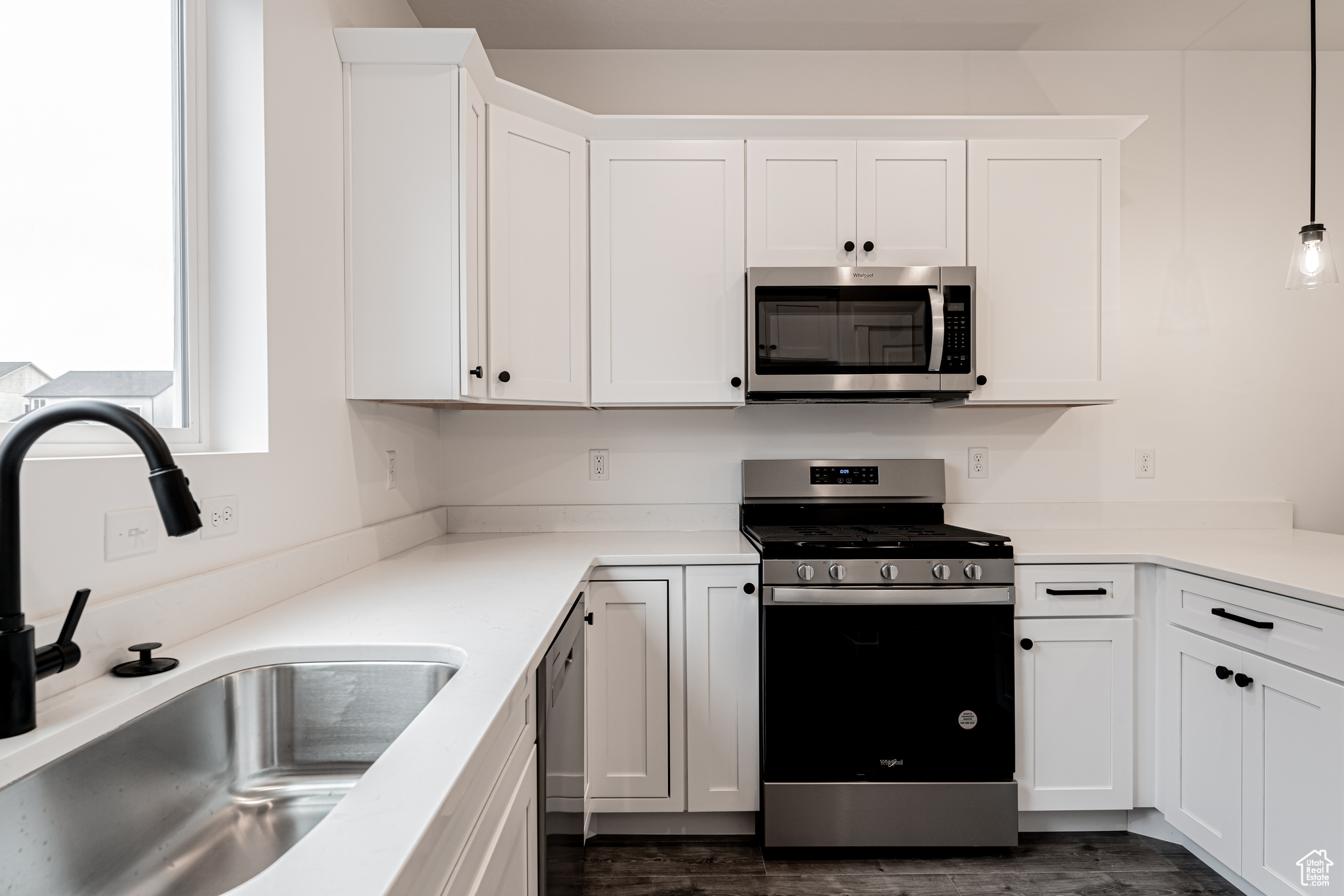 Kitchen with sink, hanging light fixtures, stainless steel appliances, dark hardwood / wood-style flooring, and white cabinets