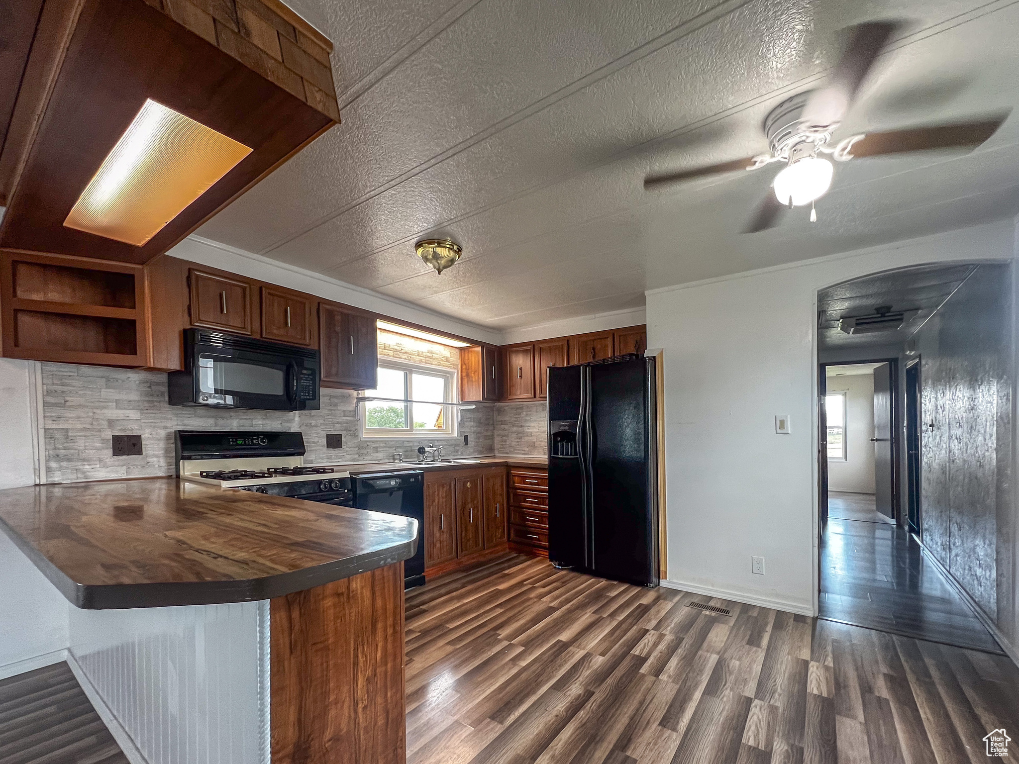 Kitchen featuring black appliances, kitchen peninsula, backsplash, dark wood-type flooring, and ceiling fan