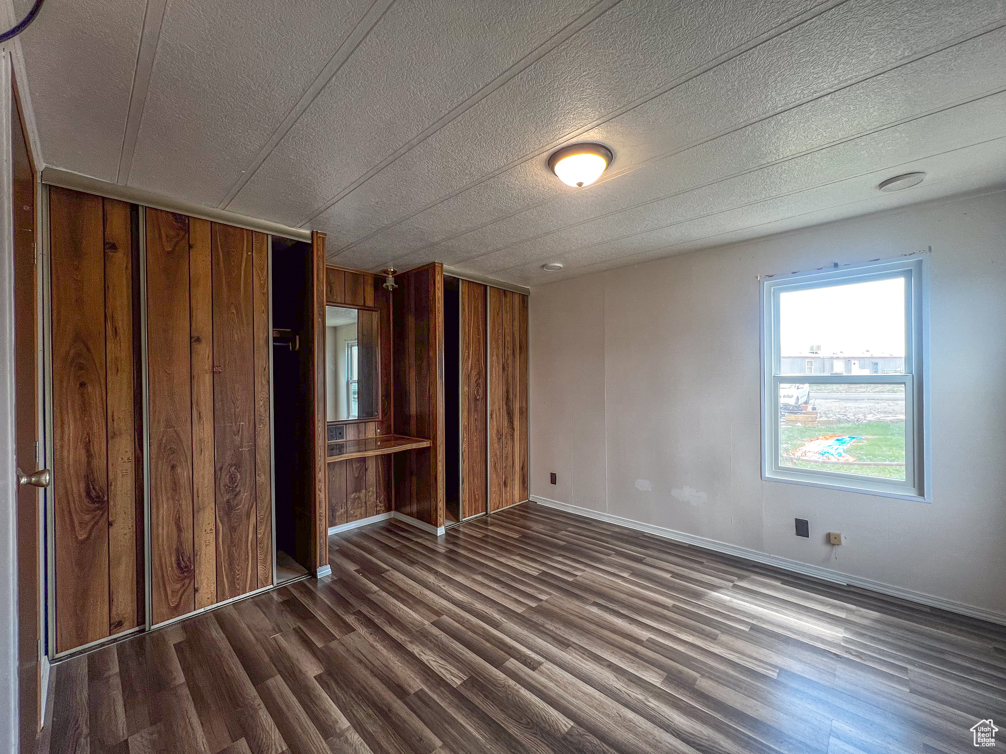 Unfurnished bedroom featuring wood walls, a closet, a textured ceiling, and dark wood-type flooring