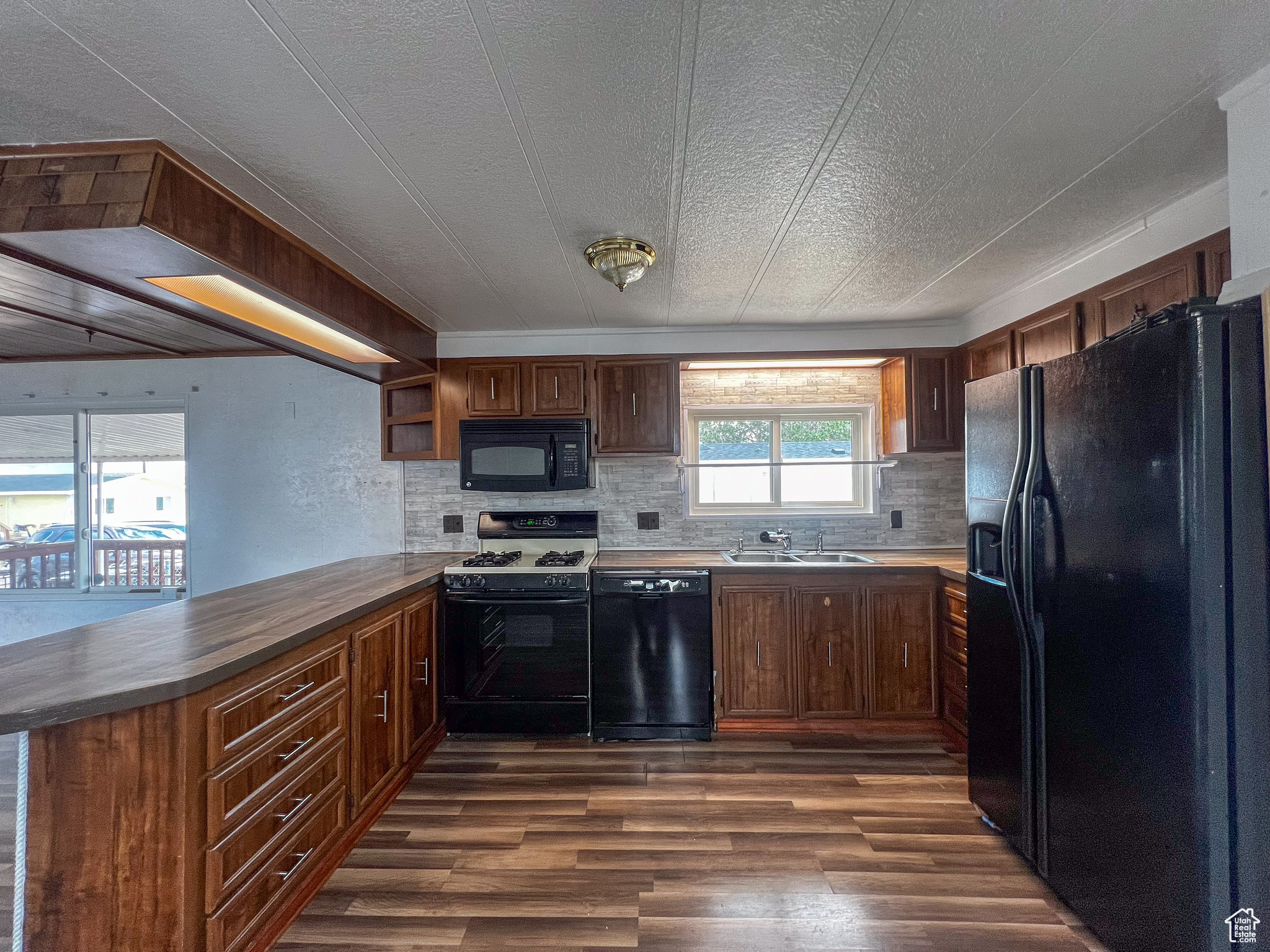 Kitchen with a textured ceiling, backsplash, dark hardwood / wood-style floors, black appliances, and sink