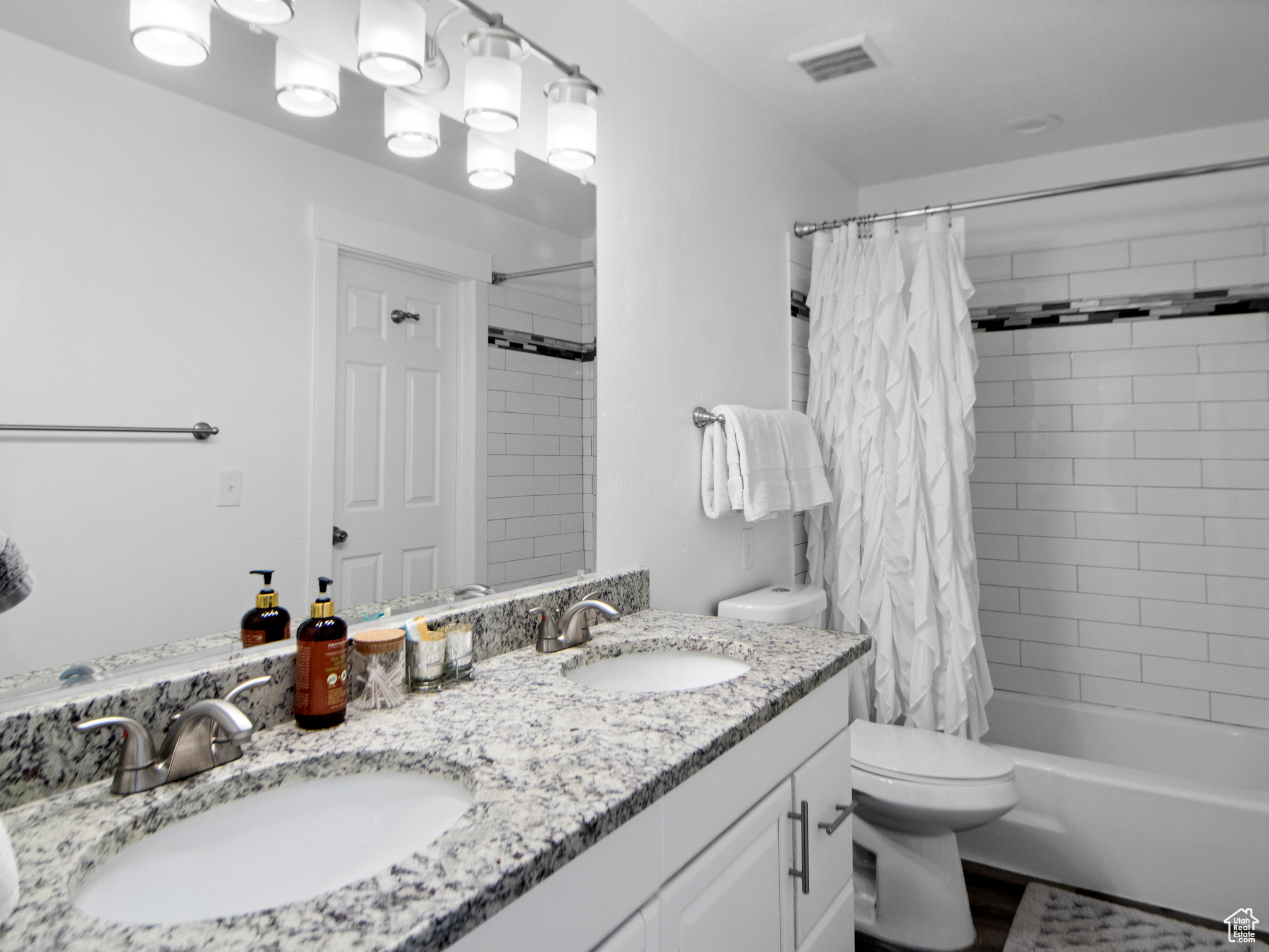 Full bathroom with double vanity, shower / bath combo, and toilet