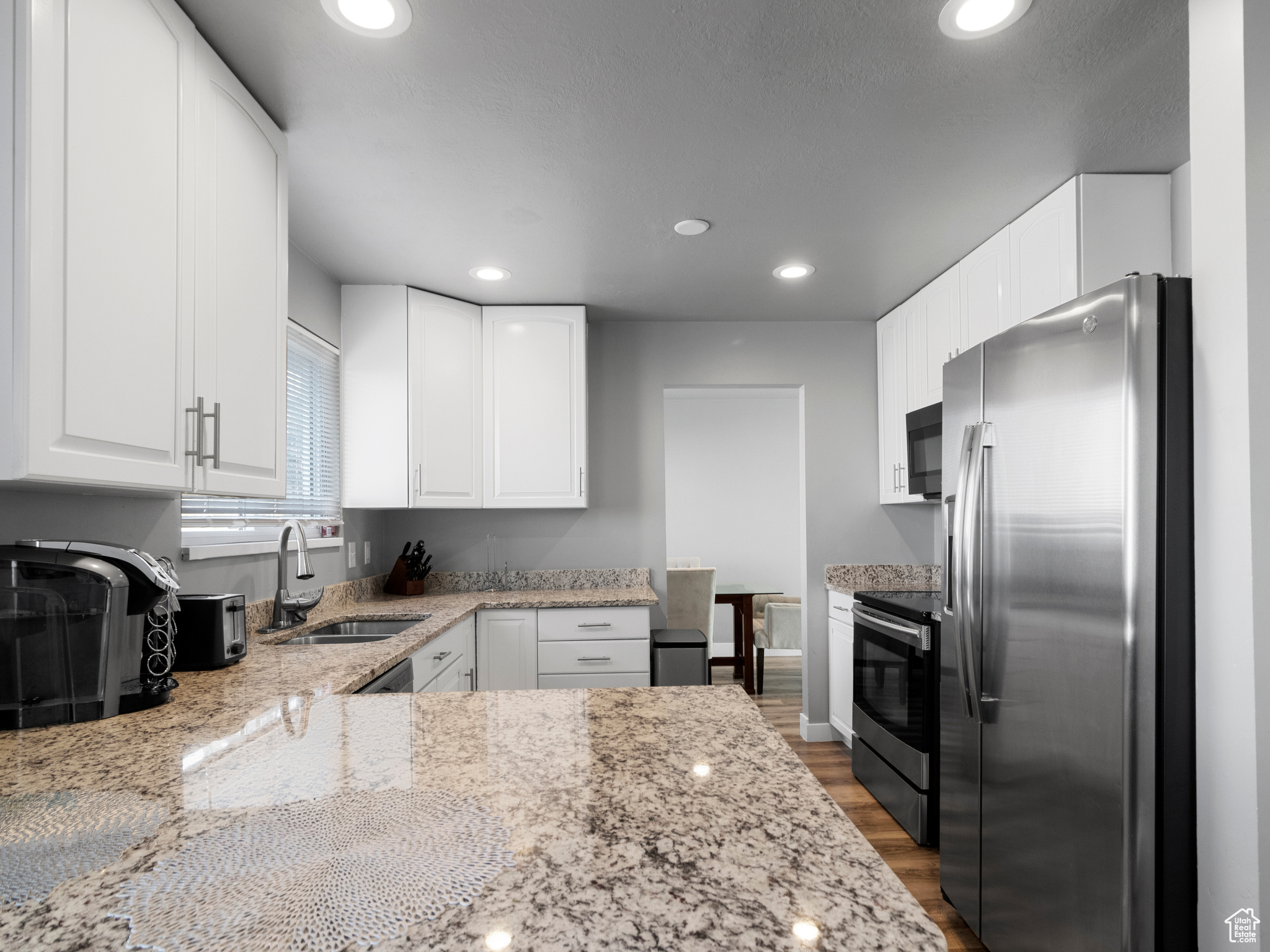 Kitchen featuring white cabinets, light stone counters, dark hardwood / wood-style flooring, appliances with stainless steel finishes, and sink