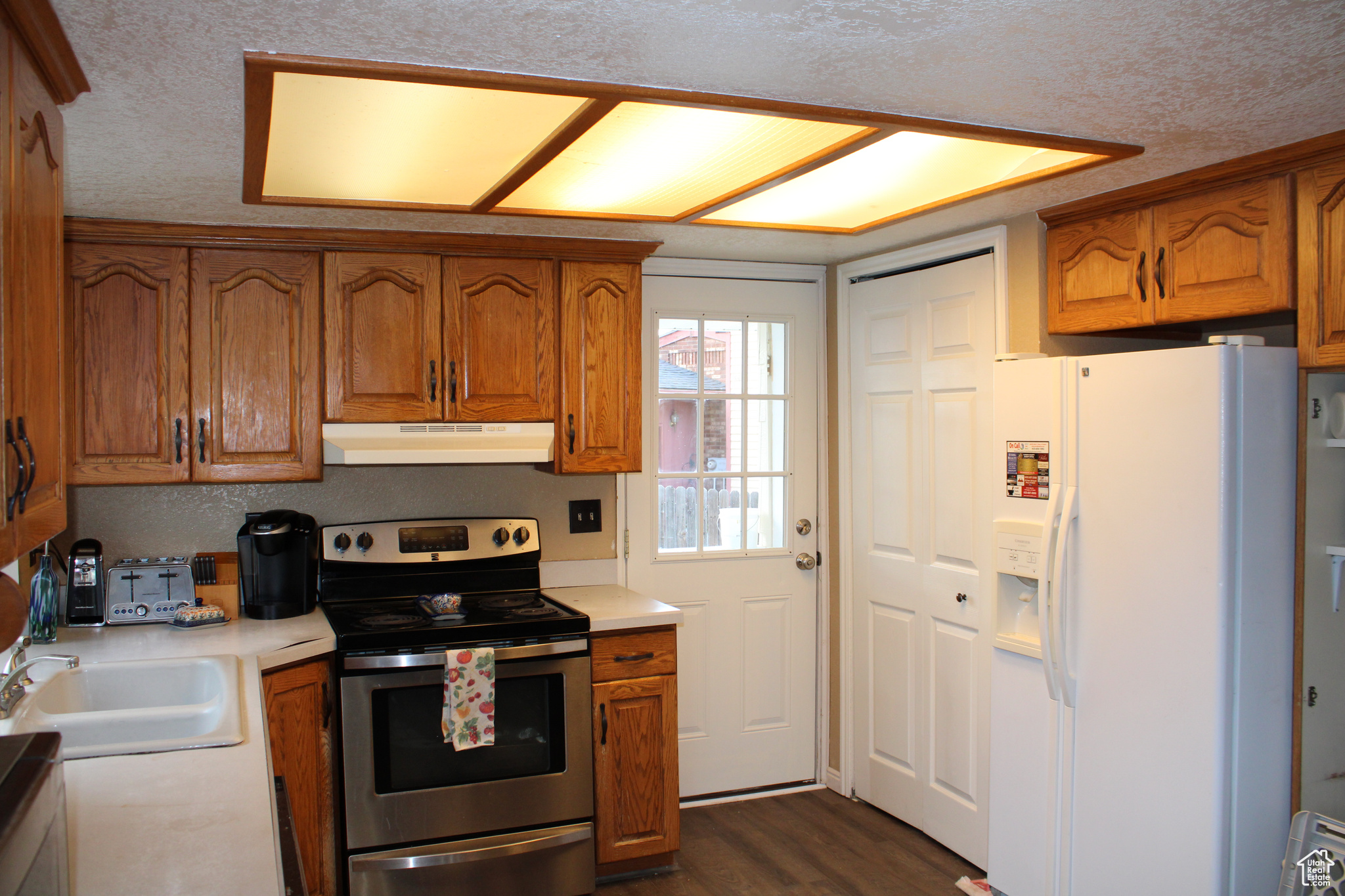 Kitchen featuring dark laminate floors, a textured ceiling, white refrigerator with ice dispenser, and stainless steel electric stove.