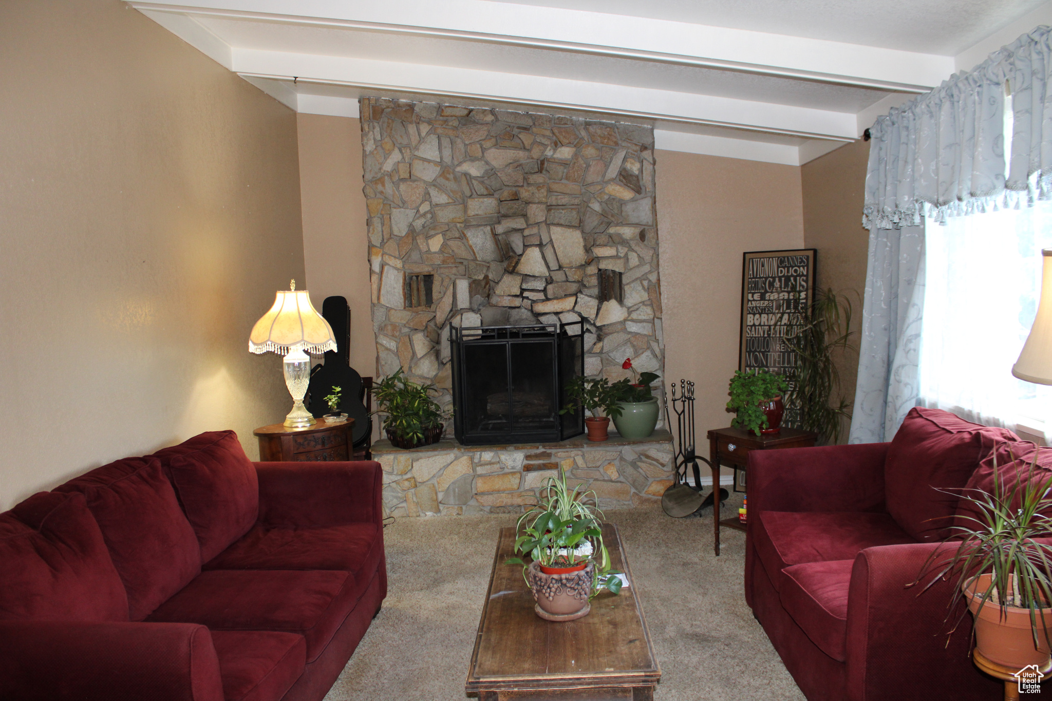 Carpeted living room with a stone fireplace and beam ceiling