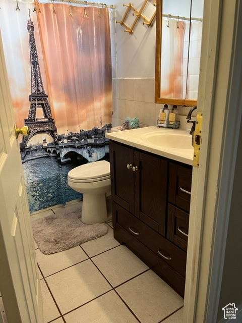 Bathroom with backsplash, toilet, vanity, tile walls, and tile floors.