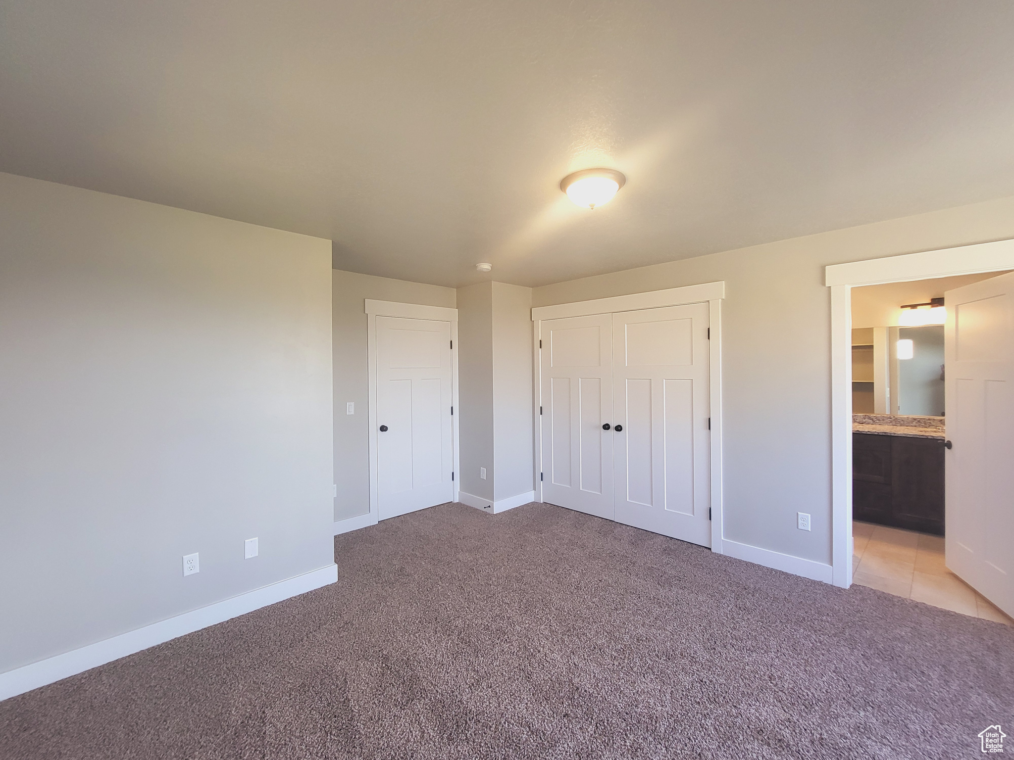 Unfurnished bedroom with a closet, connected bathroom, and light colored carpet