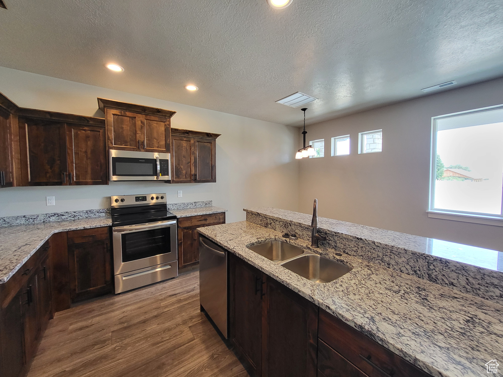 Kitchen featuring hardwood / wood-style flooring, stainless steel appliances, pendant lighting, sink, and dark brown cabinetry