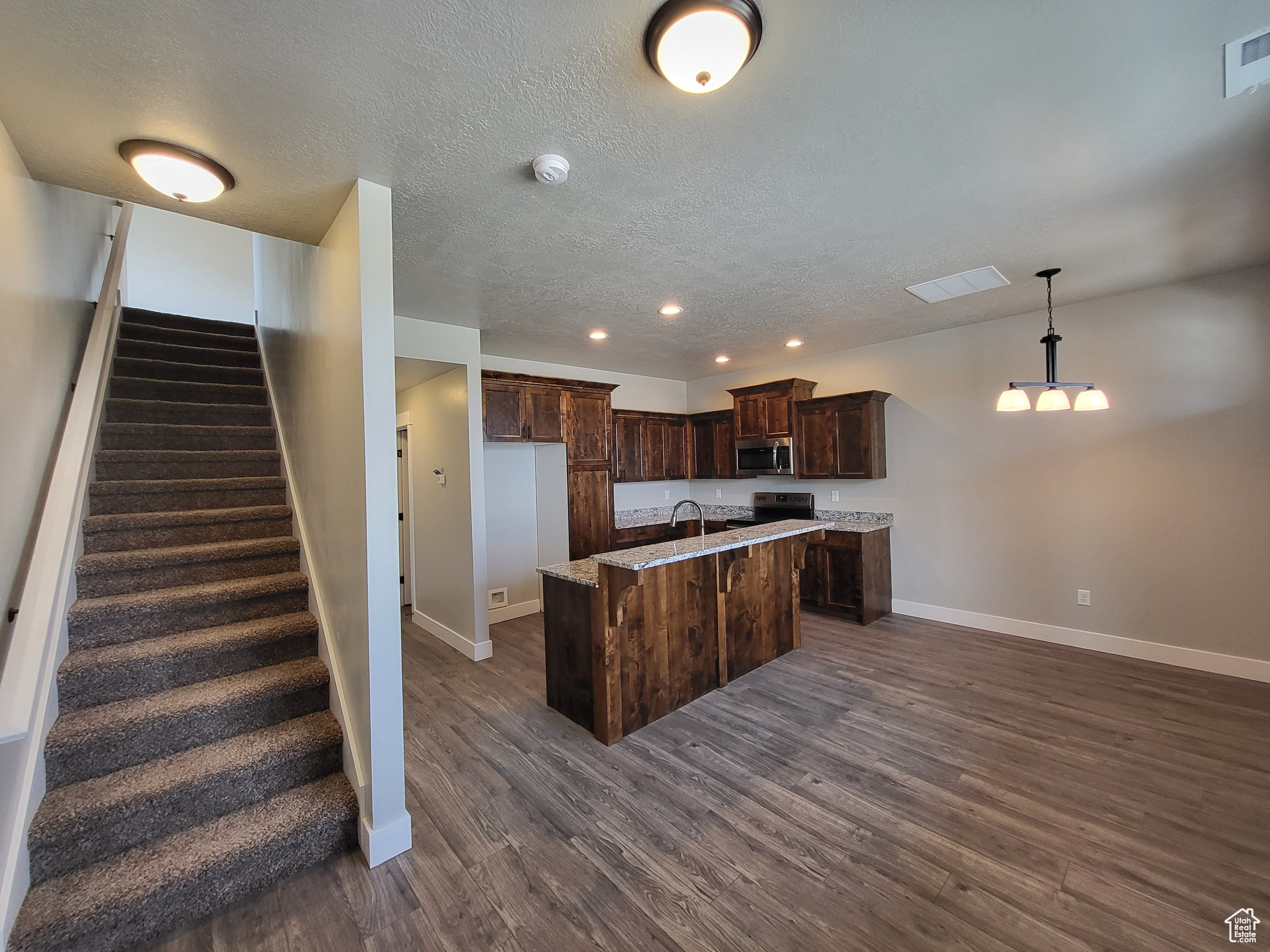 Kitchen with stove, dark brown cabinets, pendant lighting, an island with sink, and dark wood-type flooring