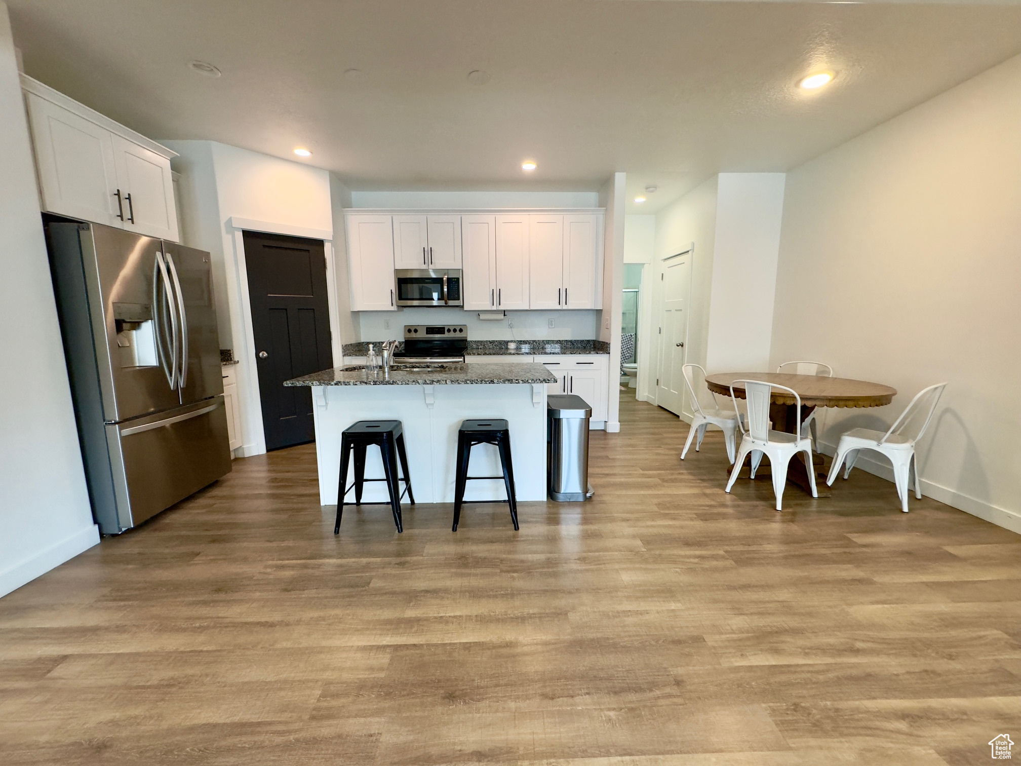 Kitchen with LVP flooring, stainless steel appliances, granite counters and white cabinets