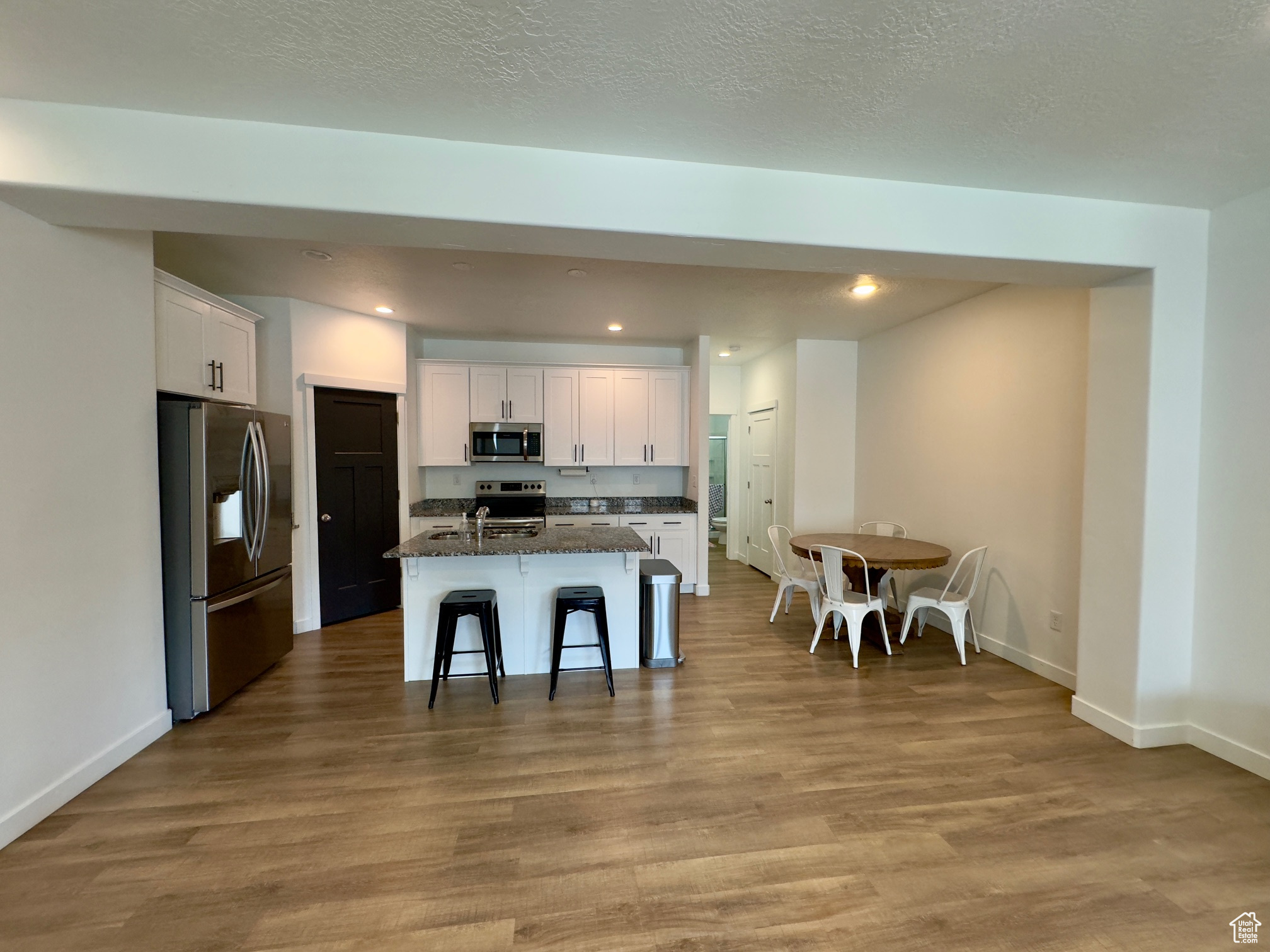 Kitchen with LVP flooring, stainless steel appliances, granite counters and white cabinets