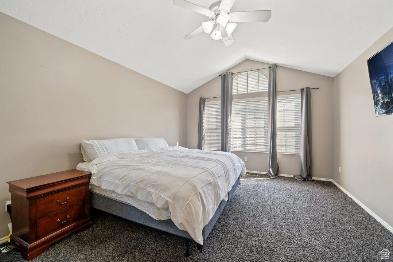 Carpeted bedroom featuring ceiling fan and vaulted ceiling