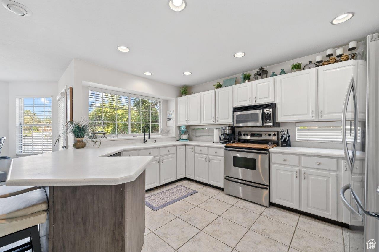 Kitchen featuring appliances with stainless steel finishes, light tile patterned floors, a wealth of natural light, and kitchen peninsula