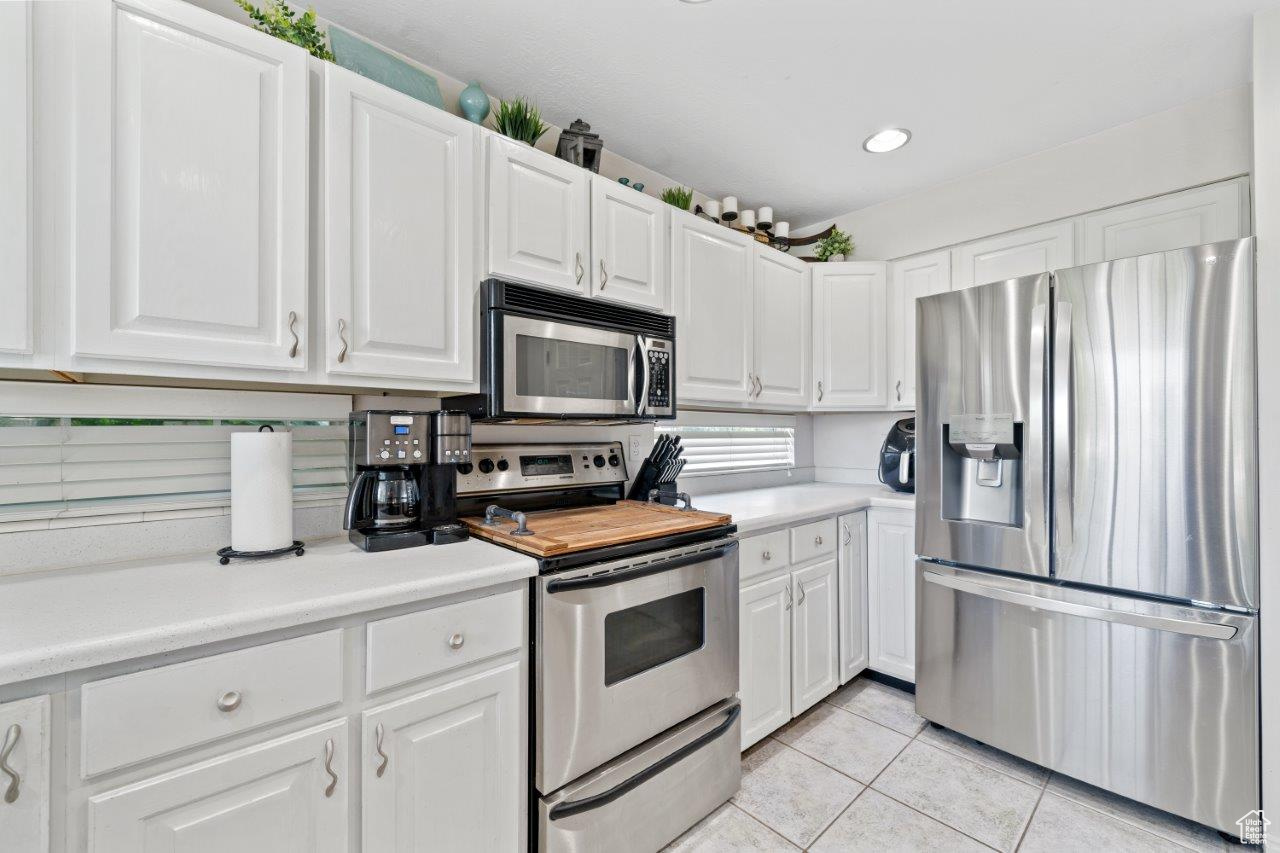 Kitchen featuring appliances with stainless steel finishes, light tile patterned floors, and white cabinets