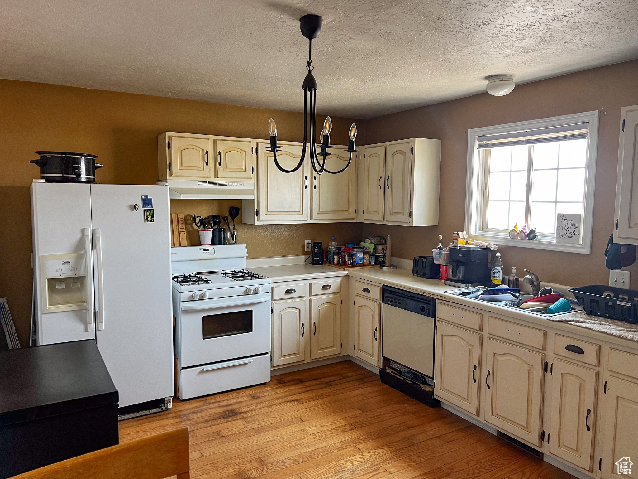 Kitchen featuring light hardwood / wood-style flooring, white appliances, an inviting chandelier, sink, and a textured ceiling