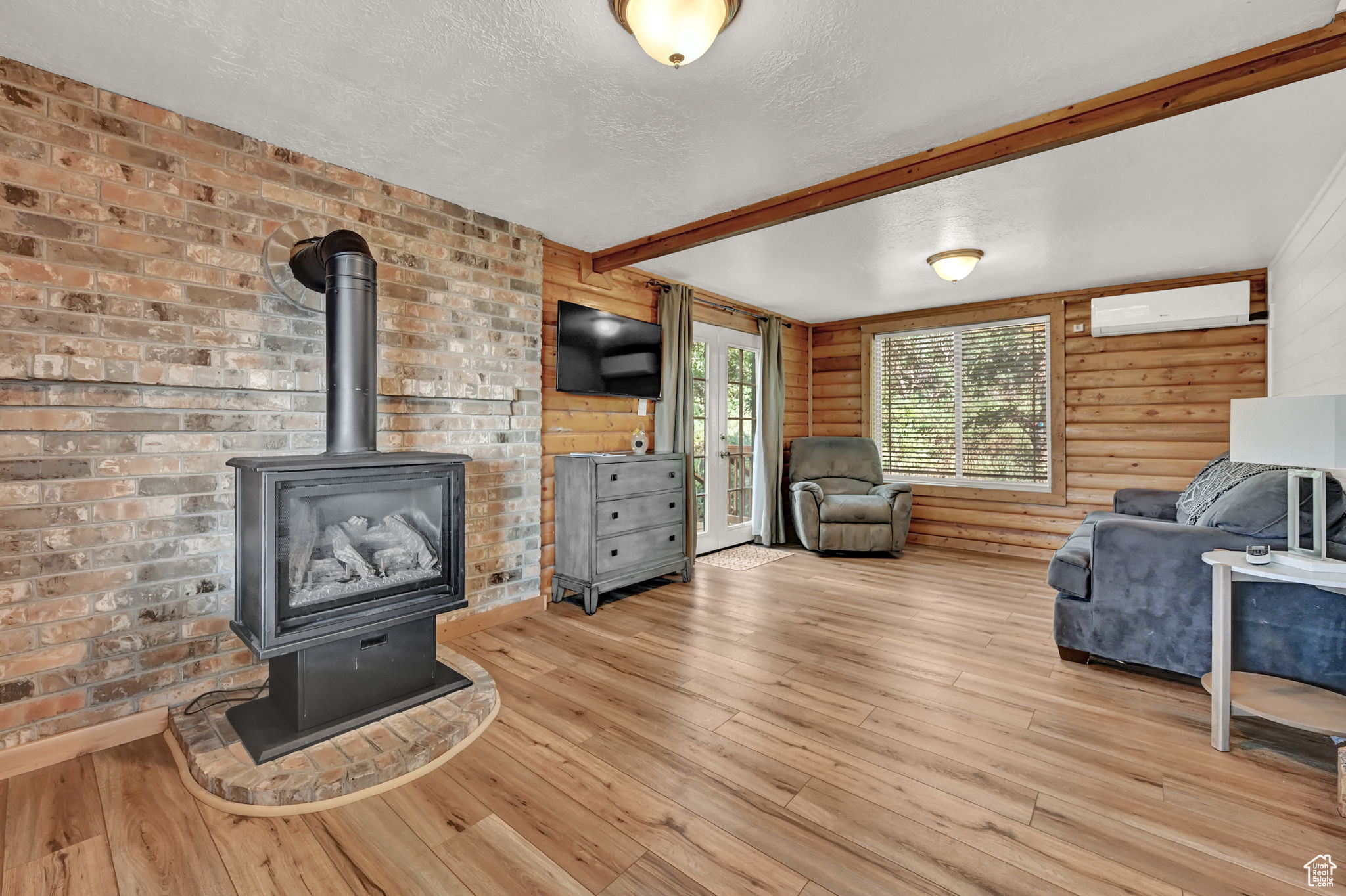 Living room with wood walls, beamed ceiling, light hardwood / wood-style flooring, and a wood stove