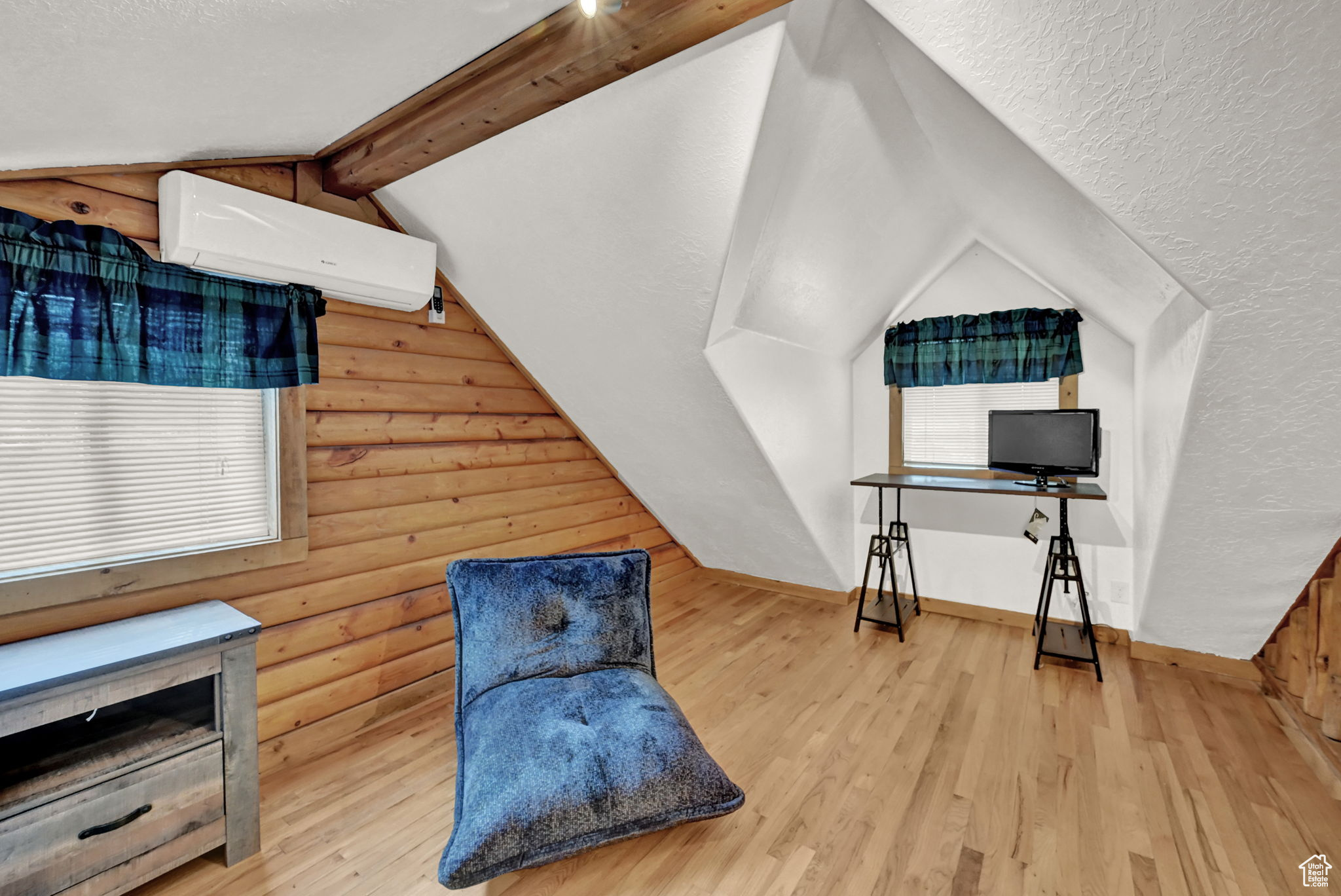 Sitting room featuring rustic walls, a wall unit AC, lofted ceiling with beams, light hardwood / wood-style flooring, and a textured ceiling