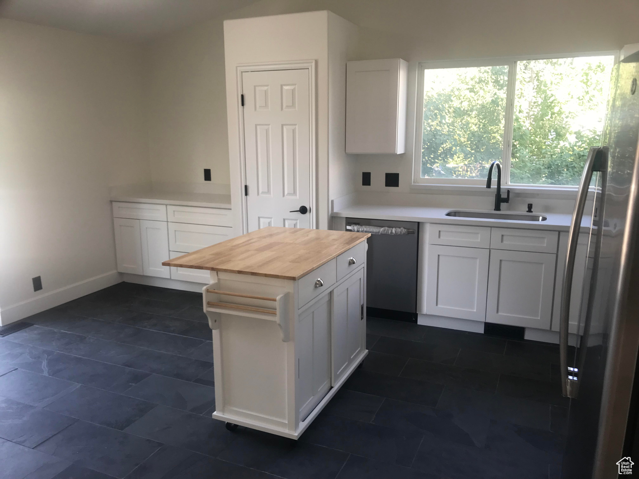 Kitchen with white cabinetry, butcher block countertops, dark tile patterned floors, sink, and appliances with stainless steel finishes