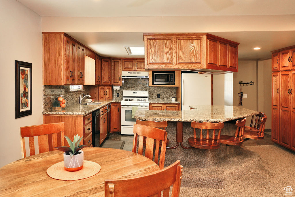 Kitchen with gas range gas stove, light stone counters, stainless steel microwave, and decorative backsplash