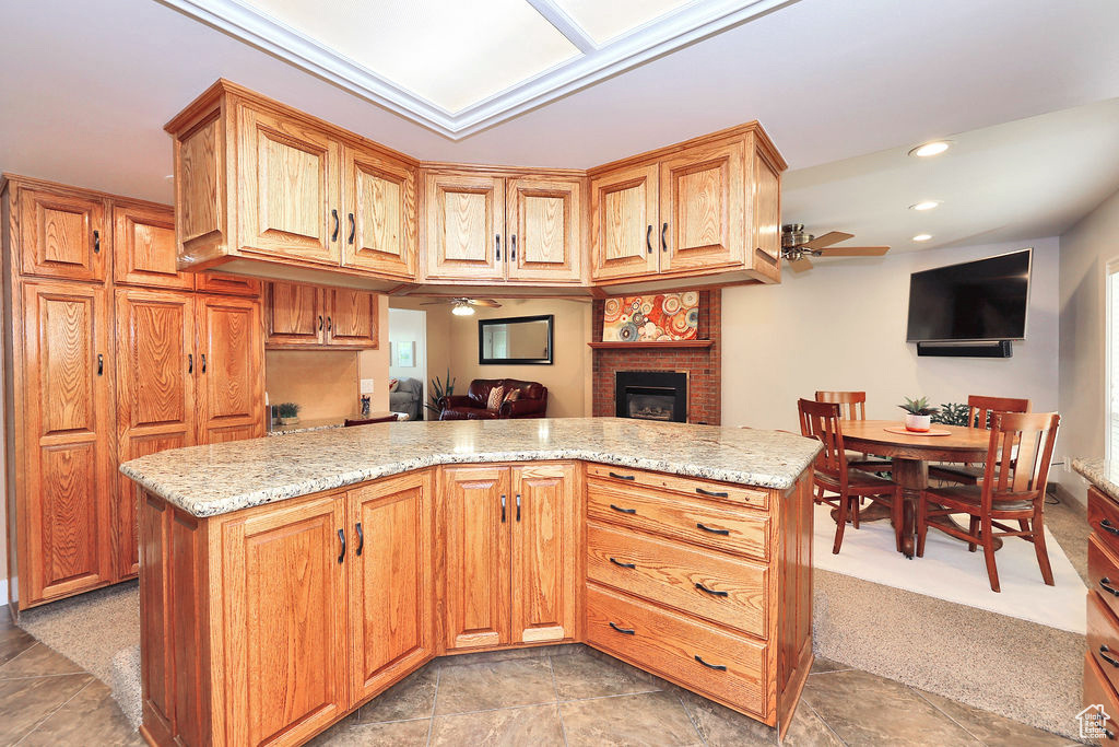 Kitchen with light stone countertops, a brick fireplace, and ceiling fan